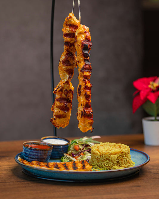 Plate of food with kabobs, rice and vegetables.