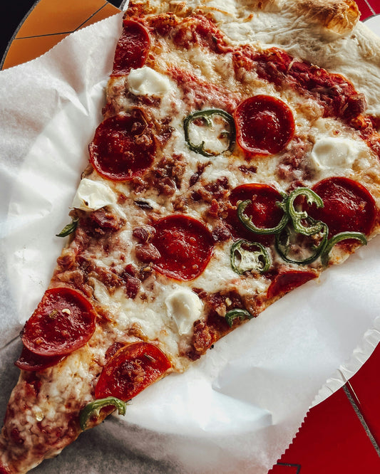 Large slice of pizza with pepperoni and jalapeños on a white napkin
