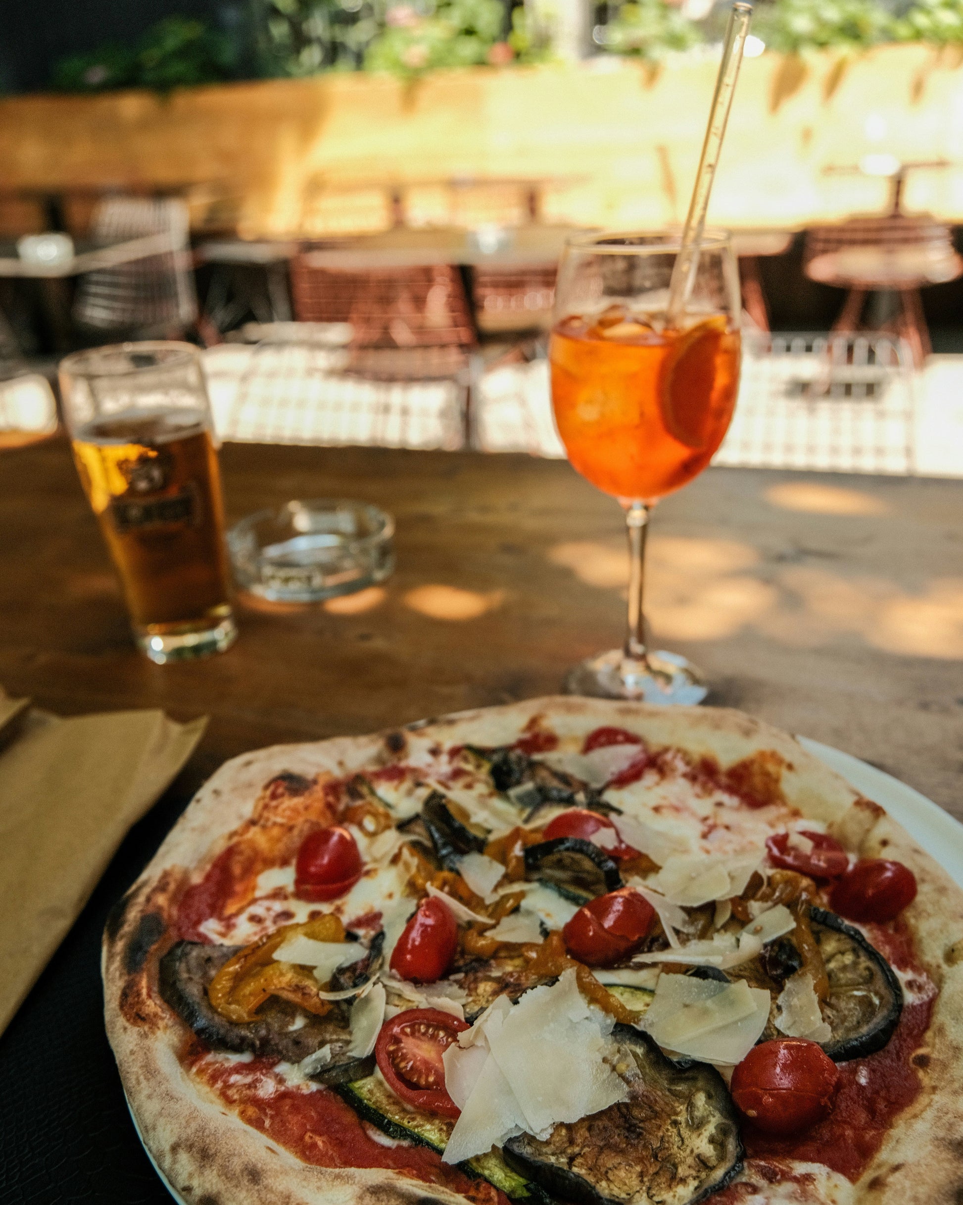 Pizza with various toppings on a table with a drink and beer glass in the background.