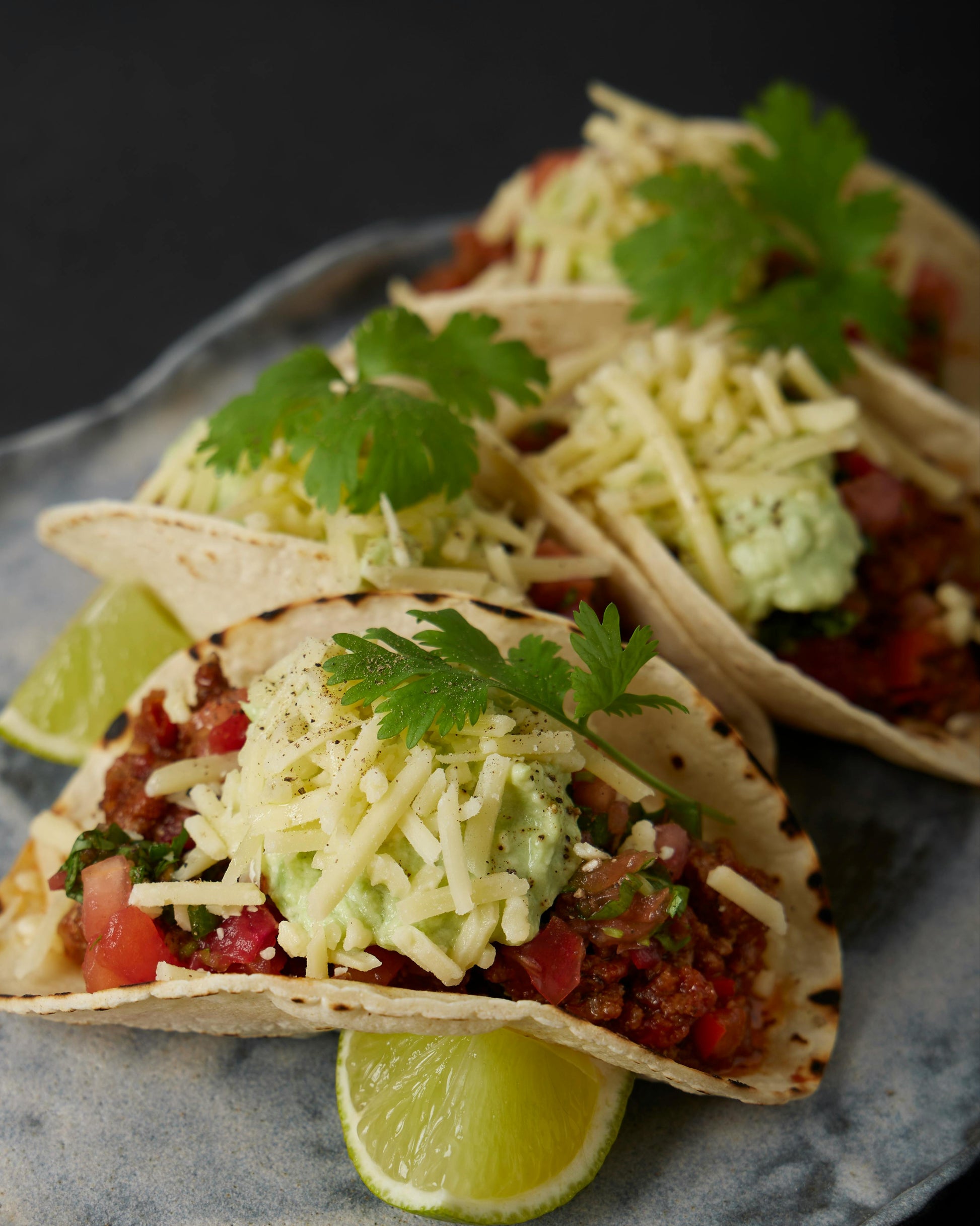 3 tacos garnished with salsa, cheese and cilantro with a side of sliced lime