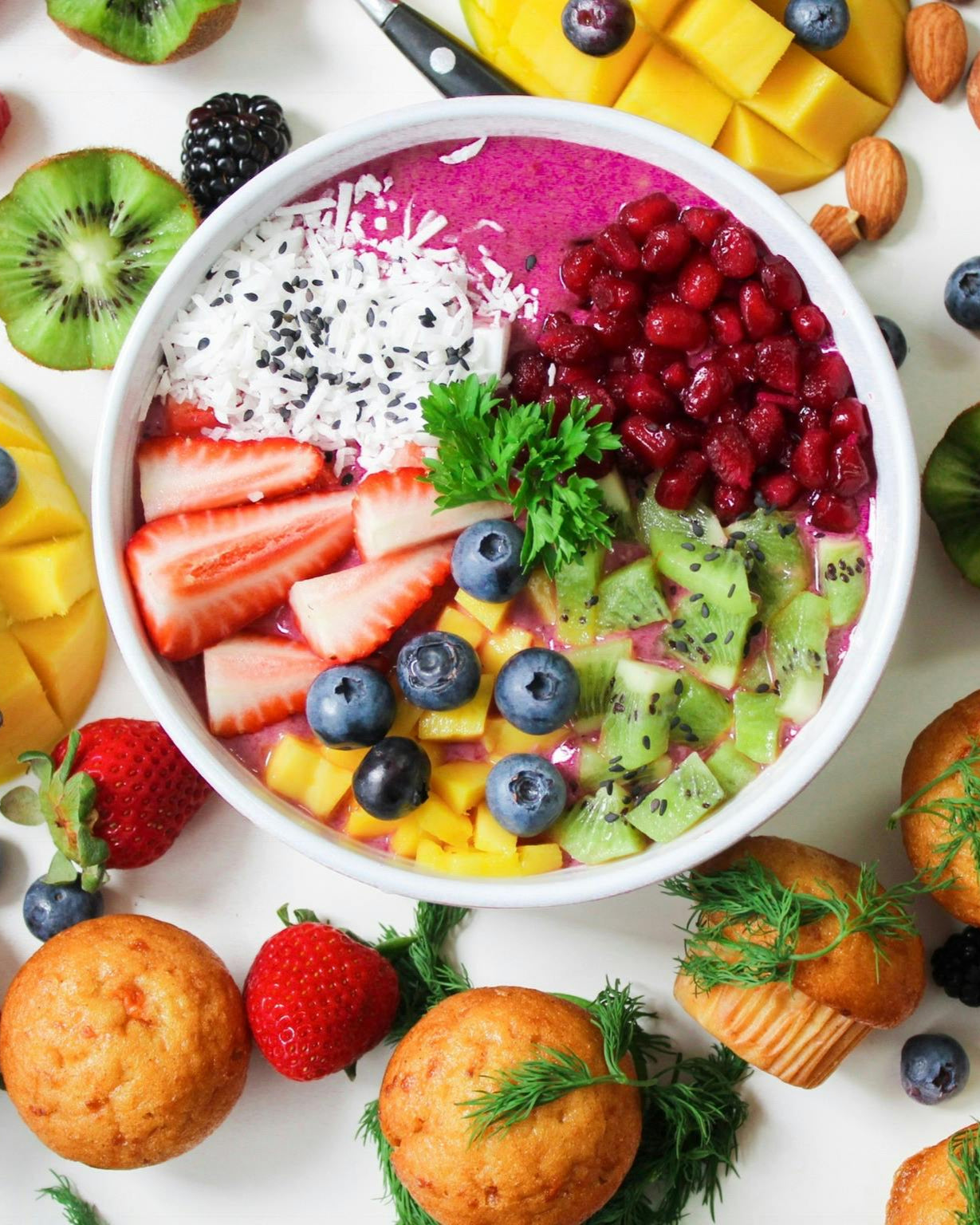 Acia bowl with fruit and muffins surrounding the bowl